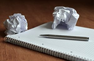 crumpled up balls of notebook paper with notebook and pen on wooden desk